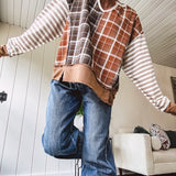 Plaid pullover pairs earth-tone mocha, cream, and rust with playful contrasting stripes on the sleeves with a split neck and relaxed fit.