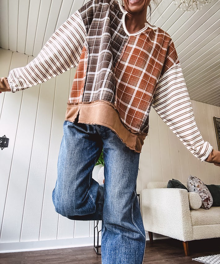 Plaid pullover pairs earth-tone mocha, cream, and rust with playful contrasting stripes on the sleeves with a split neck and relaxed fit.
