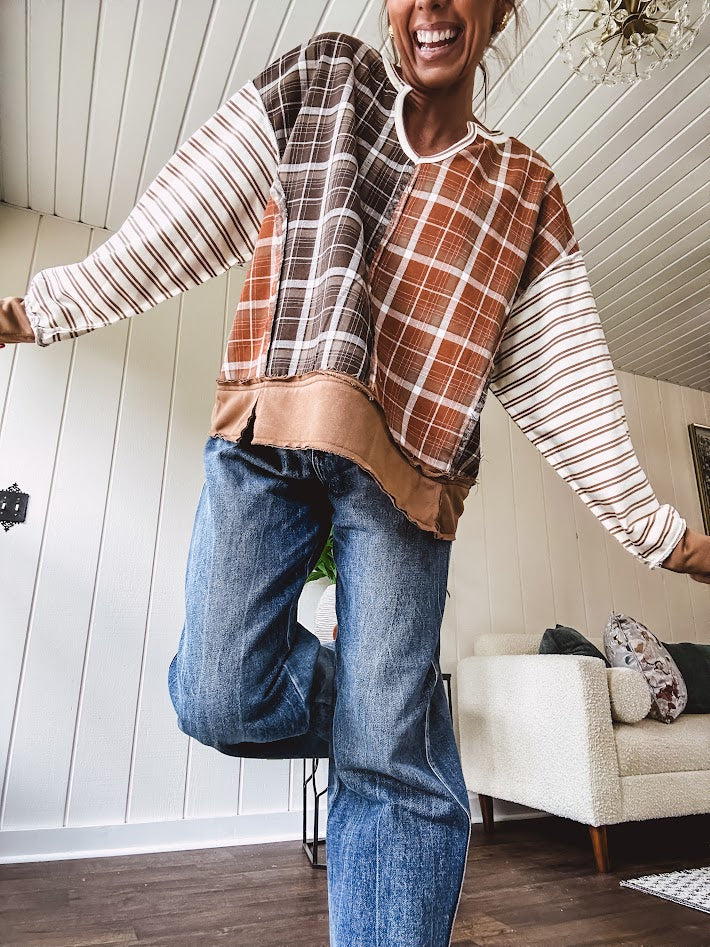 Plaid pullover pairs earth-tone mocha, cream, and rust with playful contrasting stripes on the sleeves with a split neck and relaxed fit.
