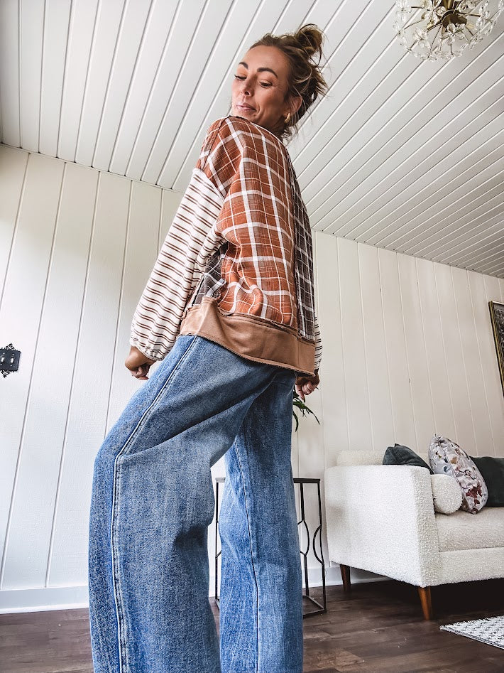 Plaid pullover pairs earth-tone mocha, cream, and rust with playful contrasting stripes on the sleeves with a split neck and relaxed fit.