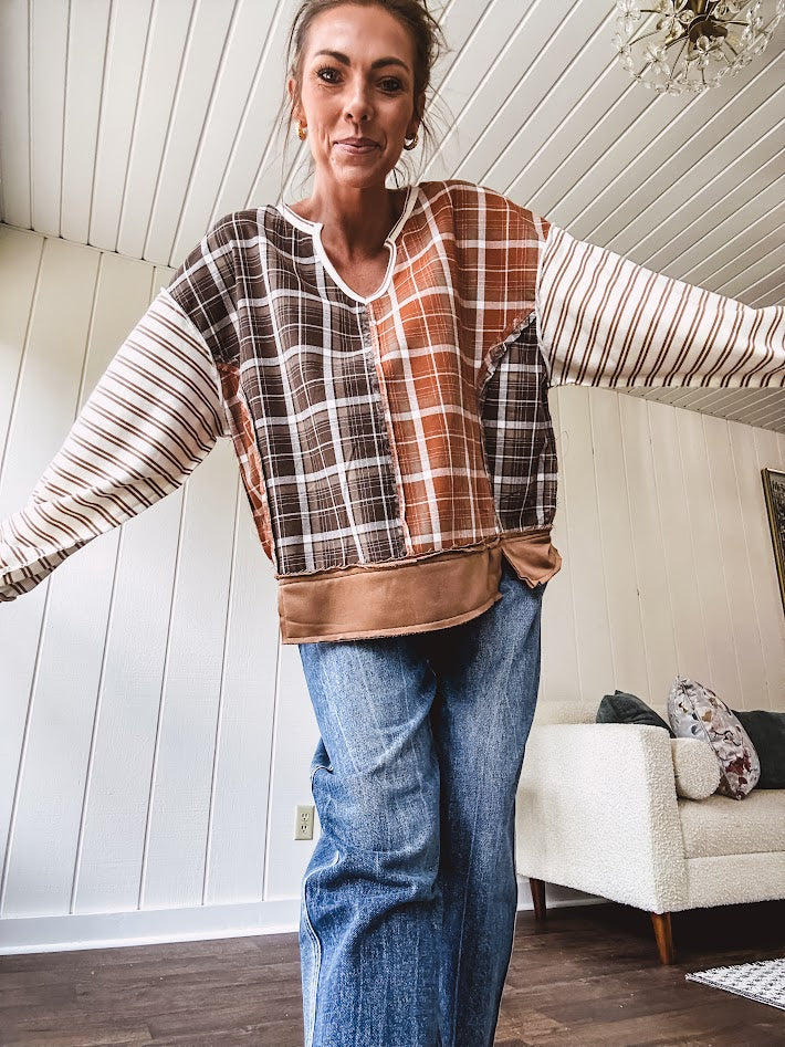 Plaid pullover pairs earth-tone mocha, cream, and rust with playful contrasting stripes on the sleeves with a split neck and relaxed fit.