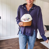 Cream canvas trucker hat with tan bill and multi colored puff embroidered lettering on the front.