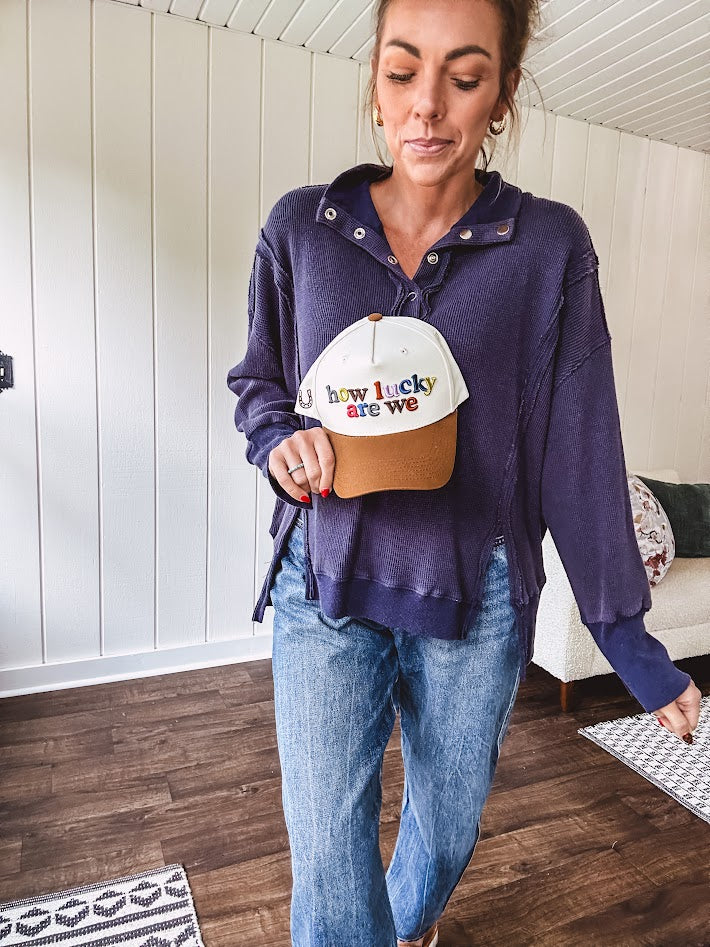 Cream canvas trucker hat with tan bill and multi colored puff embroidered lettering on the front.