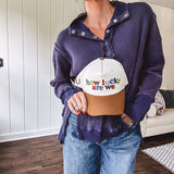 Cream canvas trucker hat with tan bill and multi colored puff embroidered lettering on the front.