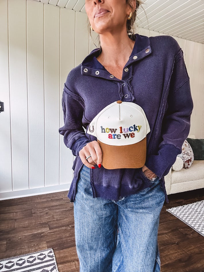 Cream canvas trucker hat with tan bill and multi colored puff embroidered lettering on the front.
