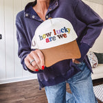 Cream canvas trucker hat with tan bill and multi colored puff embroidered lettering on the front.
