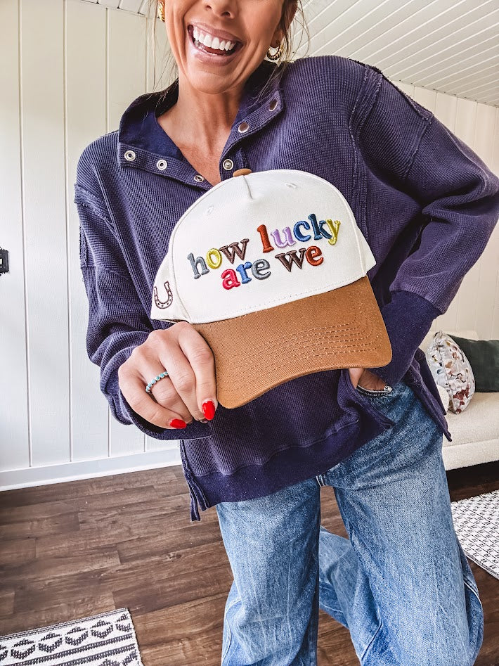 Cream canvas trucker hat with tan bill and multi colored puff embroidered lettering on the front.