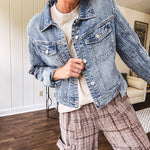 Medium wash non-stretch denim jacket with classic trim, raw, uneven hem and cuffs with silver hardware and cropped length.