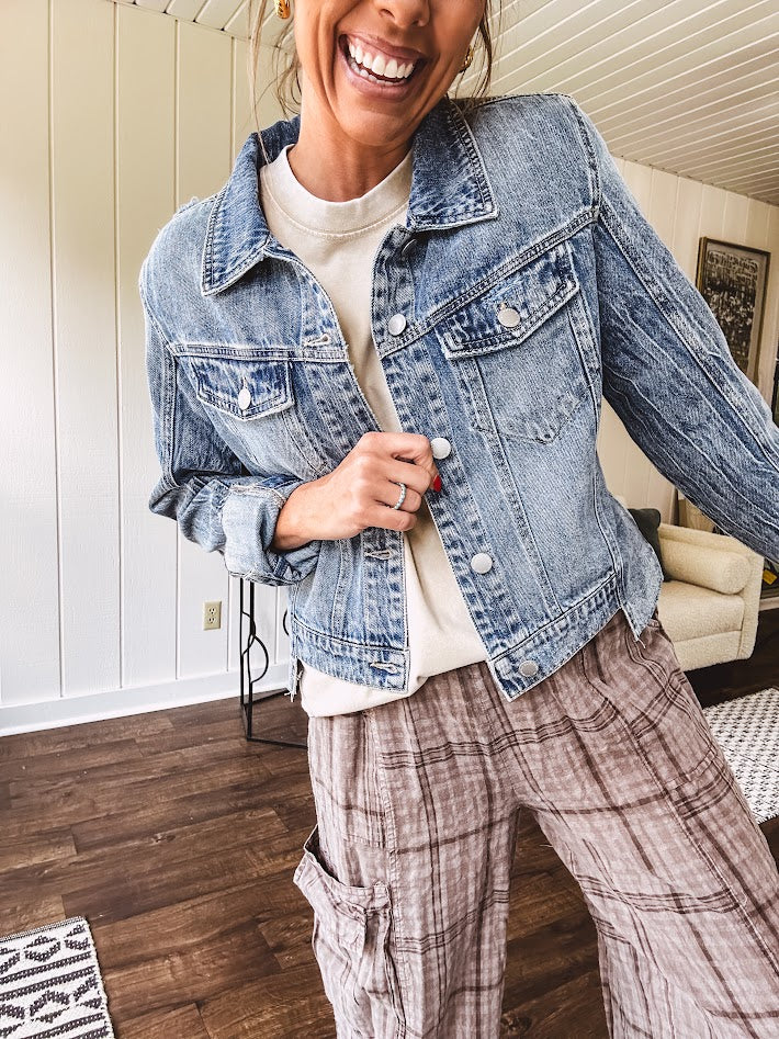Medium wash non-stretch denim jacket with classic trim, raw, uneven hem and cuffs with silver hardware and cropped length.