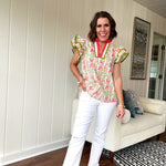 White cotton blouse with coral and lime florals and stripes at the ruffled collar and V neck, flutter sleeves with lime trim, flowy hem.