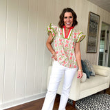 White cotton blouse with coral and lime florals and stripes at the ruffled collar and V neck, flutter sleeves with lime trim, flowy hem.