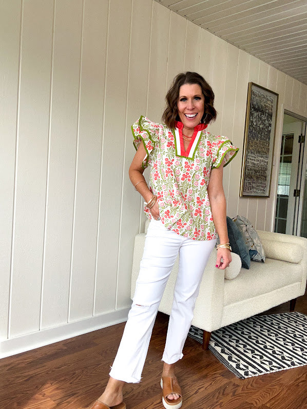 White cotton blouse with coral and lime florals and stripes at the ruffled collar and V neck, flutter sleeves with lime trim, flowy hem.