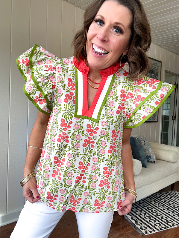 White cotton blouse with coral and lime florals and stripes at the ruffled collar and V neck, flutter sleeves with lime trim, flowy hem.