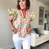 White cotton blouse with coral and lime florals and stripes at the ruffled collar and V neck, flutter sleeves with lime trim, flowy hem.