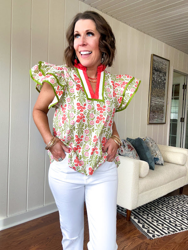 White cotton blouse with coral and lime florals and stripes at the ruffled collar and V neck, flutter sleeves with lime trim, flowy hem.