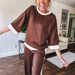 Cocoa brown super soft set with ivory trim at the round neck, cuffs and pleated side trim on the matching pants with elastic waist and pockets. 3/4 sleeve, oversized fit.