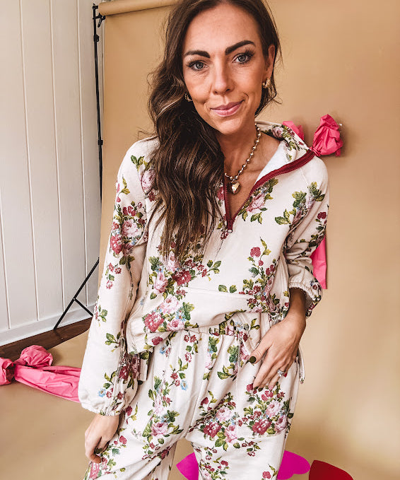 Ivory lounge set with pink, blue, and green florals, a quarter-zip top with kangaroo pocket, mock neck, and hi-low hem and matching bottoms with drawstring waist and pockets.
