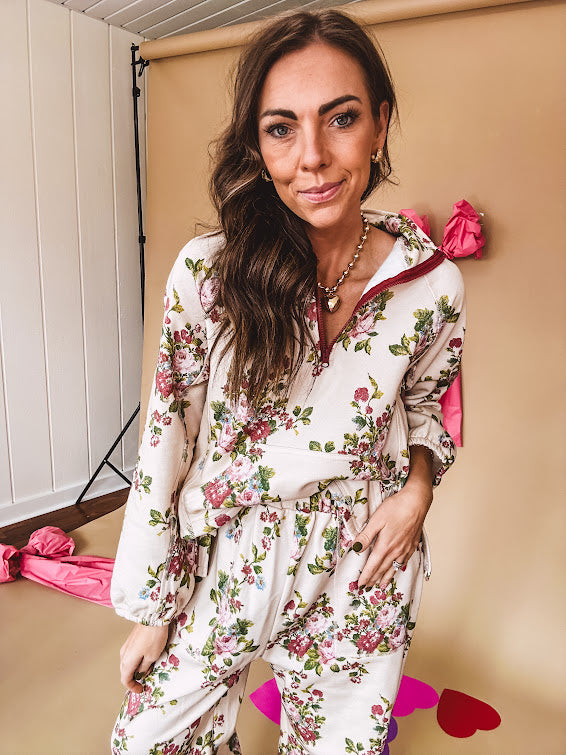 Ivory lounge set with pink, blue, and green florals, a quarter-zip top with kangaroo pocket, mock neck, and hi-low hem and matching bottoms with drawstring waist and pockets.