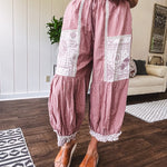 Soft, lightweight cotton pants that blend rose and grey plaid with creamy floral patchwork, lacey cream crochet trim, and a patchwork-trimmed ruffled hemline. Elastic drawstring waist and wide-leg silhouette with lace at the cuffs.