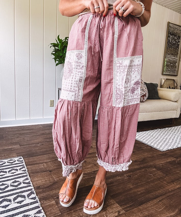 Soft, lightweight cotton pants that blend rose and grey plaid with creamy floral patchwork, lacey cream crochet trim, and a patchwork-trimmed ruffled hemline. Elastic drawstring waist and wide-leg silhouette with lace at the cuffs.
