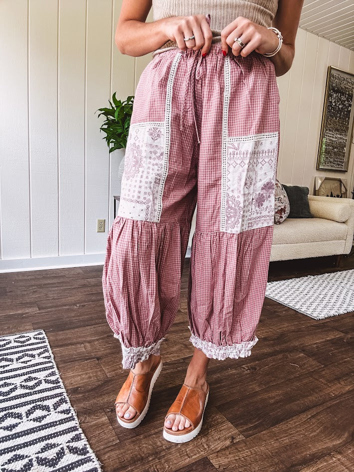 Soft, lightweight cotton pants that blend rose and grey plaid with creamy floral patchwork, lacey cream crochet trim, and a patchwork-trimmed ruffled hemline. Elastic drawstring waist and wide-leg silhouette with lace at the cuffs.