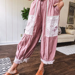 Soft, lightweight cotton pants that blend rose and grey plaid with creamy floral patchwork, lacey cream crochet trim, and a patchwork-trimmed ruffled hemline. Elastic drawstring waist and wide-leg silhouette with lace at the cuffs.
