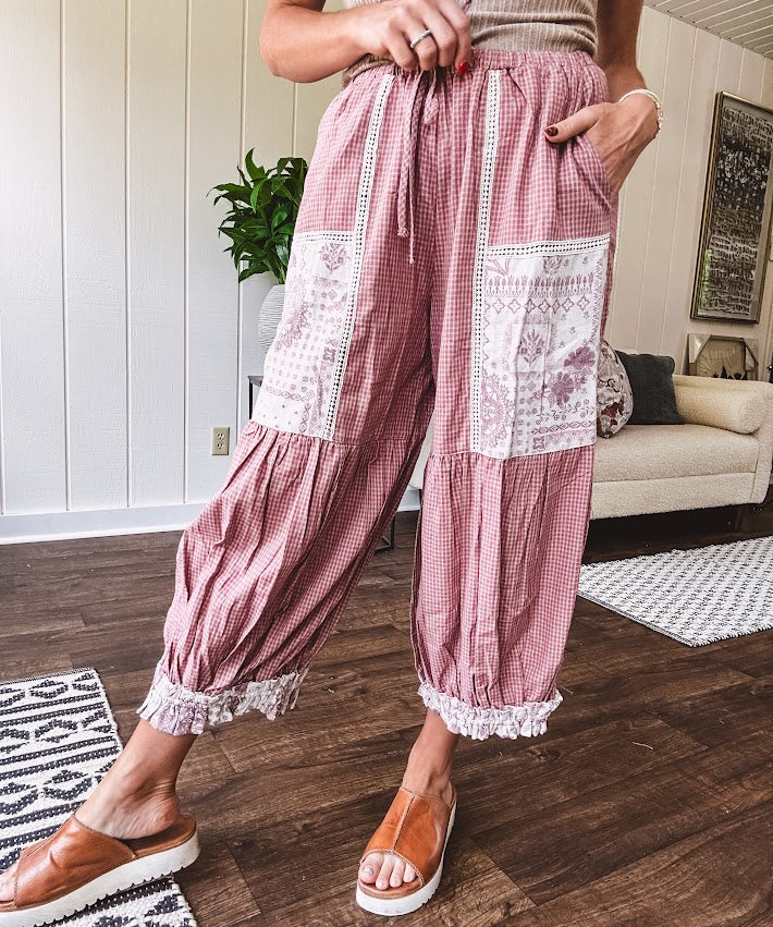 Soft, lightweight cotton pants that blend rose and grey plaid with creamy floral patchwork, lacey cream crochet trim, and a patchwork-trimmed ruffled hemline. Elastic drawstring waist and wide-leg silhouette with lace at the cuffs.