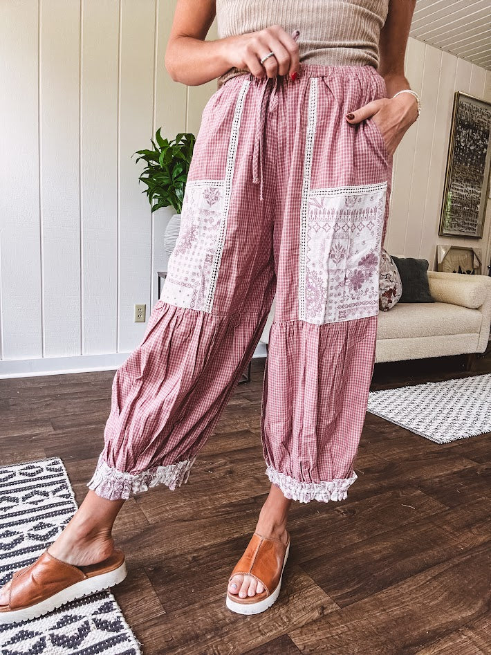 Soft, lightweight cotton pants that blend rose and grey plaid with creamy floral patchwork, lacey cream crochet trim, and a patchwork-trimmed ruffled hemline. Elastic drawstring waist and wide-leg silhouette with lace at the cuffs.