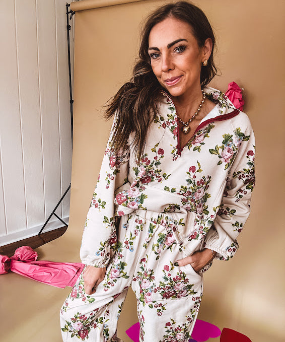 Ivory lounge set with pink, blue, and green florals, a quarter-zip top with kangaroo pocket, mock neck, and hi-low hem and matching bottoms with drawstring waist and pockets.