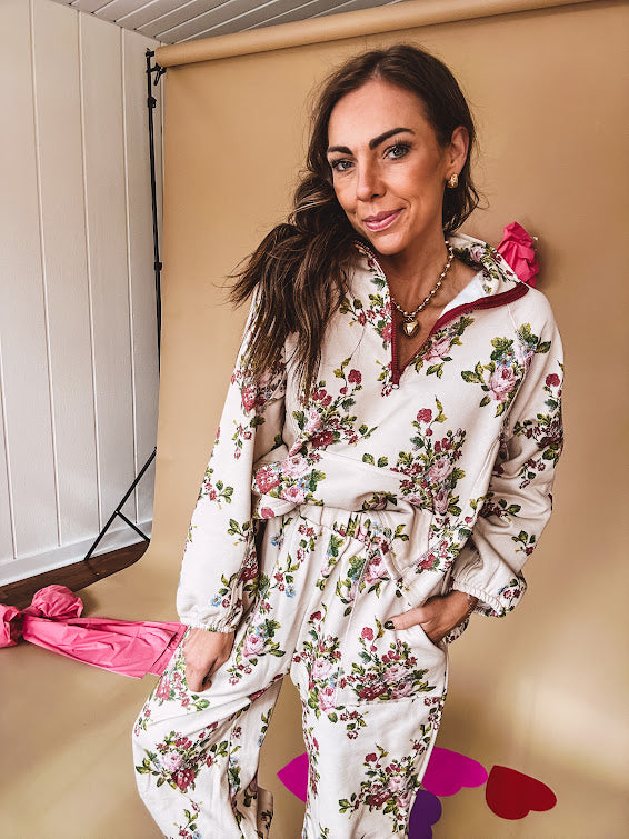 Ivory lounge set with pink, blue, and green florals, a quarter-zip top with kangaroo pocket, mock neck, and hi-low hem and matching bottoms with drawstring waist and pockets.