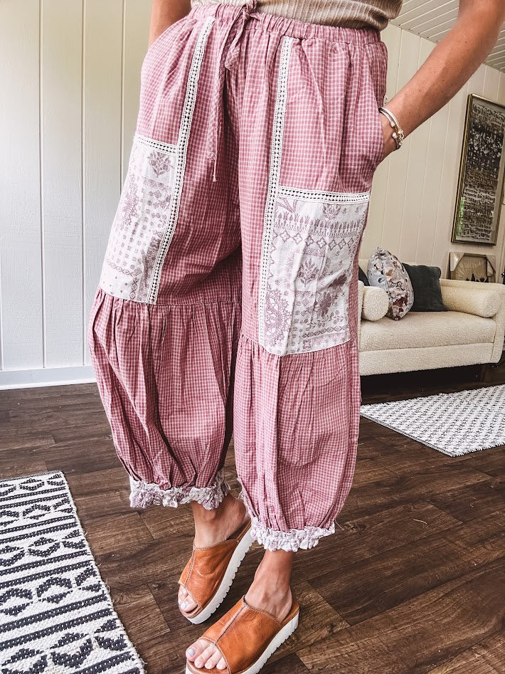 Soft, lightweight cotton pants that blend rose and grey plaid with creamy floral patchwork, lacey cream crochet trim, and a patchwork-trimmed ruffled hemline. Elastic drawstring waist and wide-leg silhouette with lace at the cuffs.