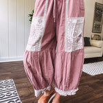 Soft, lightweight cotton pants that blend rose and grey plaid with creamy floral patchwork, lacey cream crochet trim, and a patchwork-trimmed ruffled hemline. Elastic drawstring waist and wide-leg silhouette with lace at the cuffs.