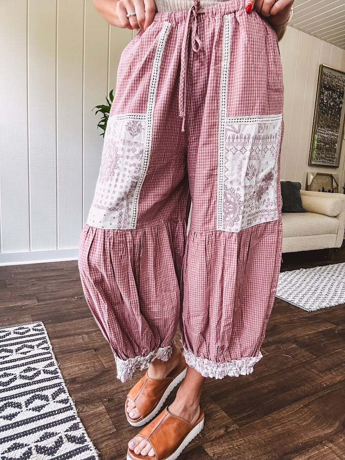 Soft, lightweight cotton pants that blend rose and grey plaid with creamy floral patchwork, lacey cream crochet trim, and a patchwork-trimmed ruffled hemline. Elastic drawstring waist and wide-leg silhouette with lace at the cuffs.