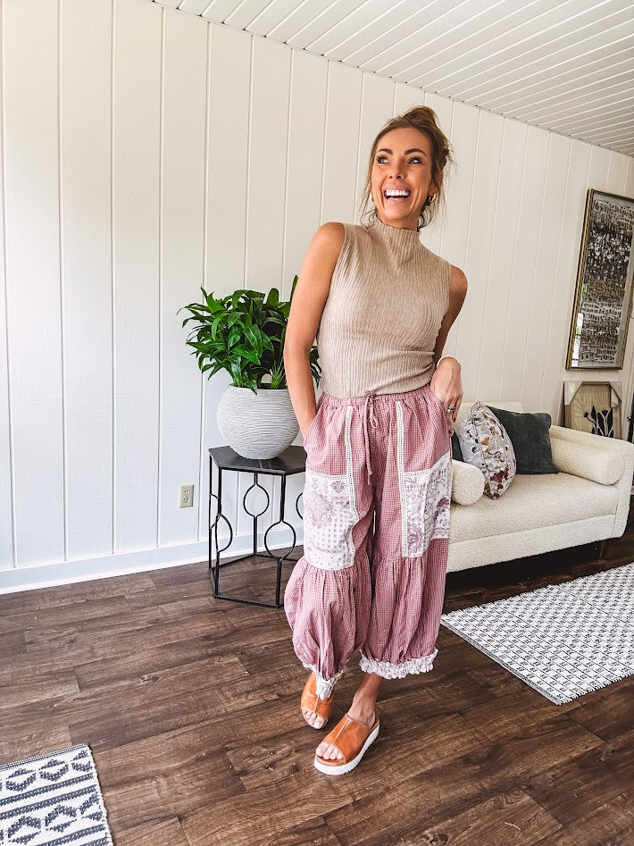 Soft, lightweight cotton pants that blend rose and grey plaid with creamy floral patchwork, lacey cream crochet trim, and a patchwork-trimmed ruffled hemline. Elastic drawstring waist and wide-leg silhouette with lace at the cuffs.