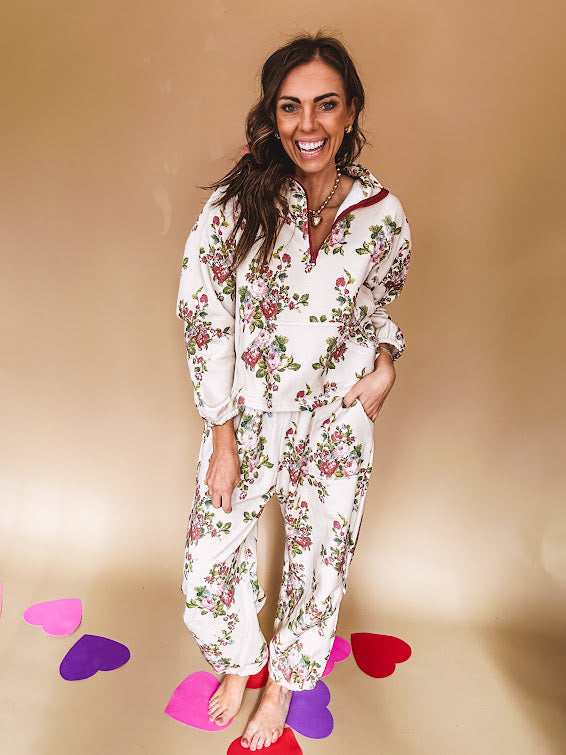 Ivory lounge set with pink, blue, and green florals, a quarter-zip top with kangaroo pocket, mock neck, and hi-low hem and matching bottoms with drawstring waist and pockets.