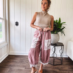 Soft, lightweight cotton pants that blend rose and grey plaid with creamy floral patchwork, lacey cream crochet trim, and a patchwork-trimmed ruffled hemline. Elastic drawstring waist and wide-leg silhouette with lace at the cuffs.