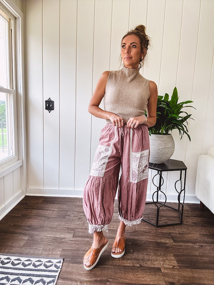 Soft, lightweight cotton pants that blend rose and grey plaid with creamy floral patchwork, lacey cream crochet trim, and a patchwork-trimmed ruffled hemline. Elastic drawstring waist and wide-leg silhouette with lace at the cuffs.