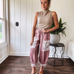 Soft, lightweight cotton pants that blend rose and grey plaid with creamy floral patchwork, lacey cream crochet trim, and a patchwork-trimmed ruffled hemline. Elastic drawstring waist and wide-leg silhouette with lace at the cuffs.