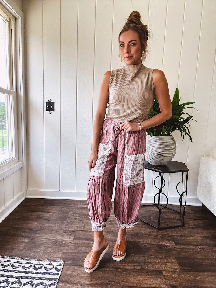 Soft, lightweight cotton pants that blend rose and grey plaid with creamy floral patchwork, lacey cream crochet trim, and a patchwork-trimmed ruffled hemline. Elastic drawstring waist and wide-leg silhouette with lace at the cuffs.
