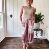 Soft, lightweight cotton pants that blend rose and grey plaid with creamy floral patchwork, lacey cream crochet trim, and a patchwork-trimmed ruffled hemline. Elastic drawstring waist and wide-leg silhouette with lace at the cuffs.