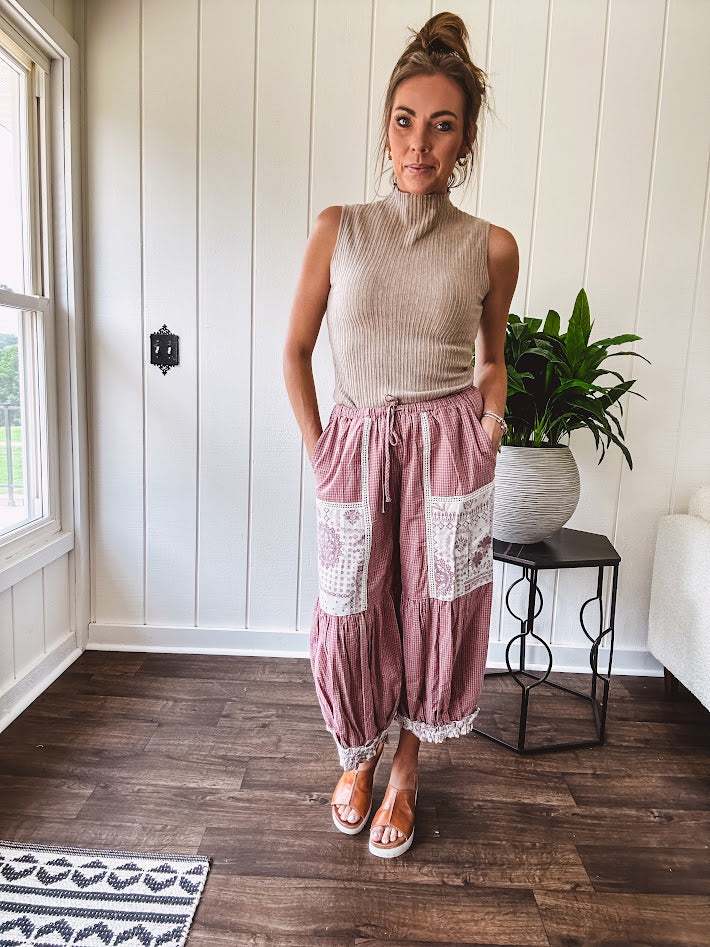Soft, lightweight cotton pants that blend rose and grey plaid with creamy floral patchwork, lacey cream crochet trim, and a patchwork-trimmed ruffled hemline. Elastic drawstring waist and wide-leg silhouette with lace at the cuffs.
