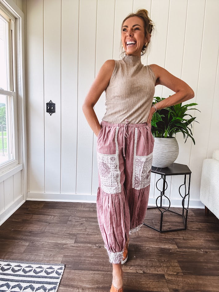 Soft, lightweight cotton pants that blend rose and grey plaid with creamy floral patchwork, lacey cream crochet trim, and a patchwork-trimmed ruffled hemline. Elastic drawstring waist and wide-leg silhouette with lace at the cuffs.