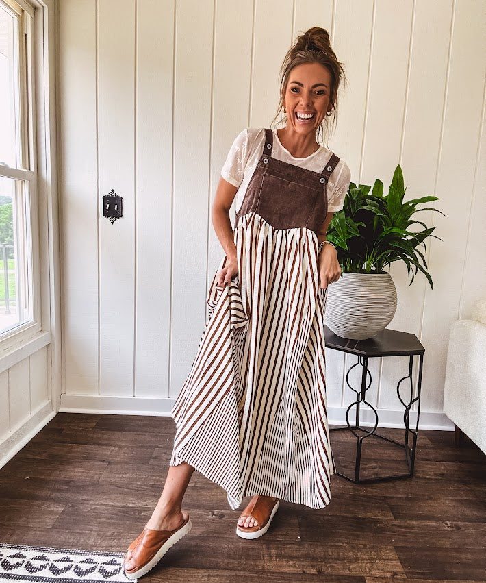 Brown washed denim overall top with silver metal hardware and adjustable straps and a cream and brown striped, lightweight skirt with pockets.