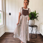 Brown washed denim overall top with silver metal hardware and adjustable straps and a cream and brown striped, lightweight skirt with pockets.