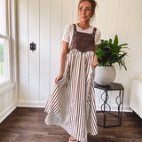 Brown washed denim overall top with silver metal hardware and adjustable straps and a cream and brown striped, lightweight skirt with pockets.