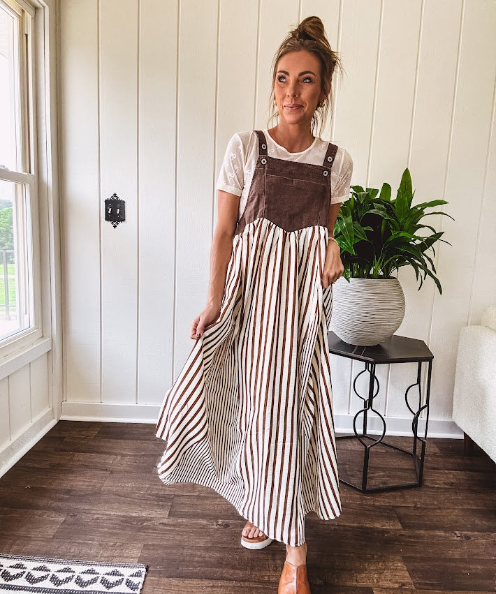 Brown washed denim overall top with silver metal hardware and adjustable straps and a cream and brown striped, lightweight skirt with pockets.