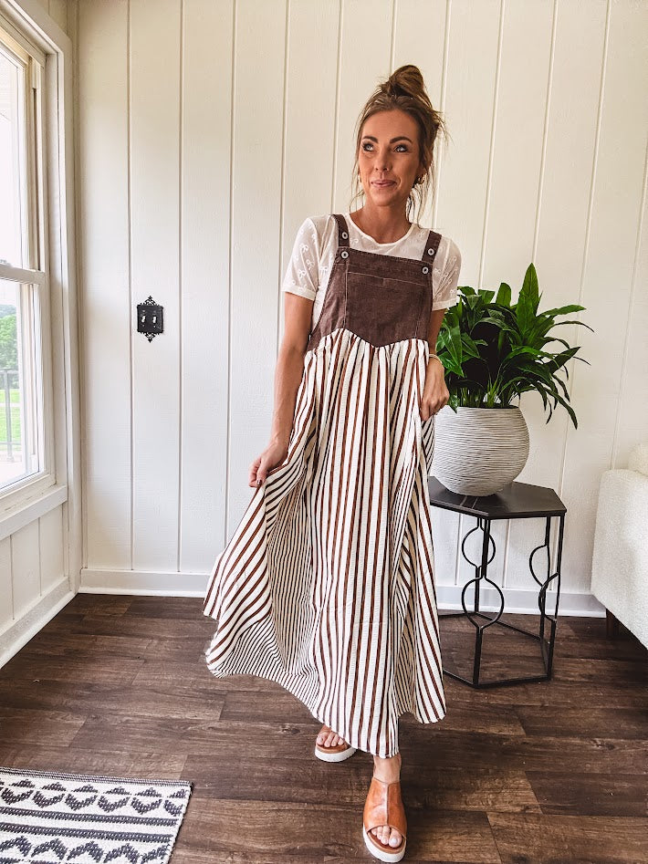 Brown washed denim overall top with silver metal hardware and adjustable straps and a cream and brown striped, lightweight skirt with pockets.