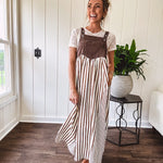 Brown washed denim overall top with silver metal hardware and adjustable straps and a cream and brown striped, lightweight skirt with pockets.