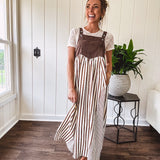 Brown washed denim overall top with silver metal hardware and adjustable straps and a cream and brown striped, lightweight skirt with pockets.