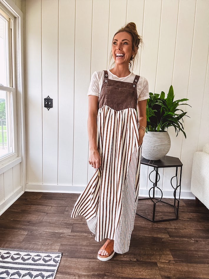 Brown washed denim overall top with silver metal hardware and adjustable straps and a cream and brown striped, lightweight skirt with pockets.